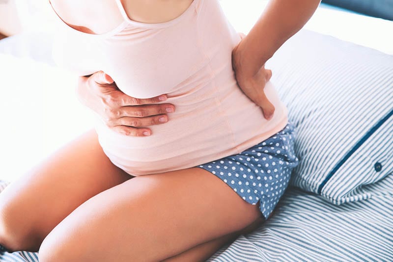 Junge schwangere Frau fühlt Wehe auf dem Bett