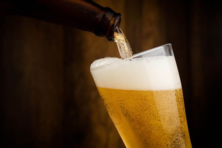 Einschenken von kühlem Bier aus der Flasche in ein Glas auf dem Holztisch