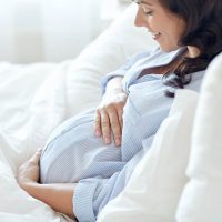 glückliche schwangere Frau streichelt Bauch im Bett