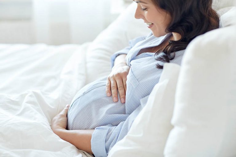 glückliche schwangere Frau streichelt Bauch im Bett