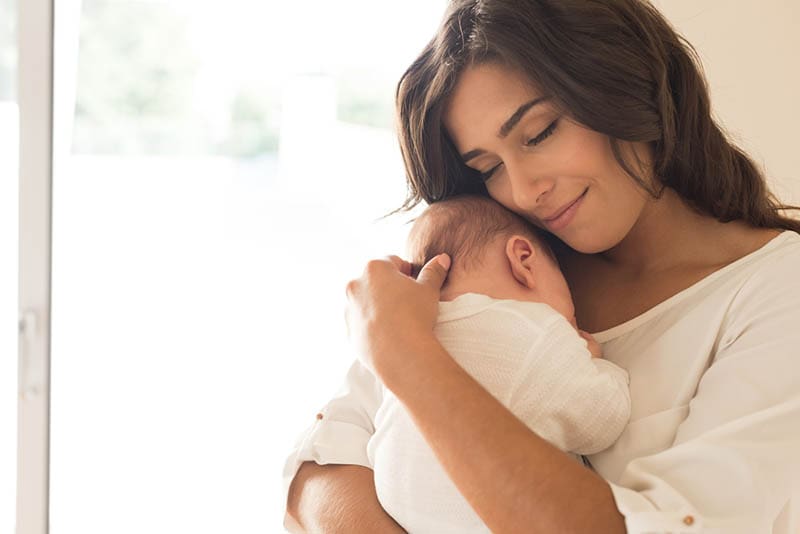 glückliche Mutter hält ihr neugeborenes Baby auf der Brust im Schlafzimmer