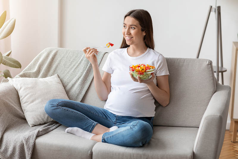 glückliche schwangere Frau essen auf der Couch zu Hause