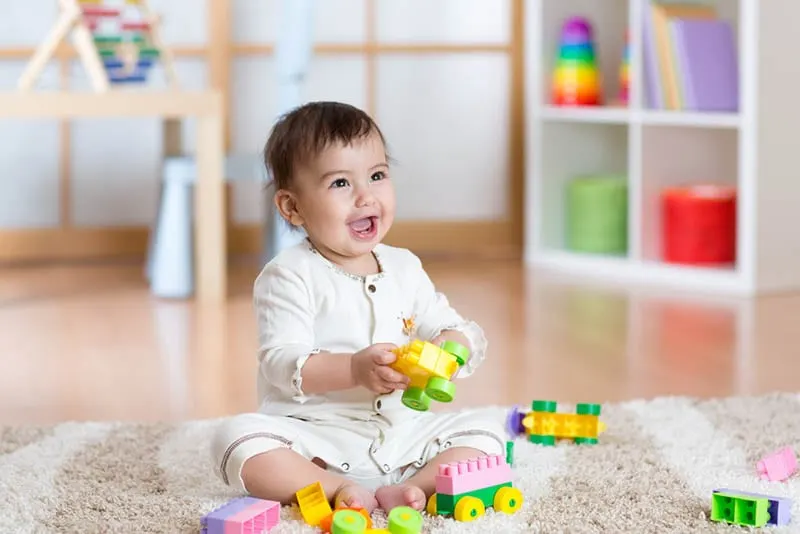 glückliches Baby spielt mit Lego-Würfeln auf dem Boden