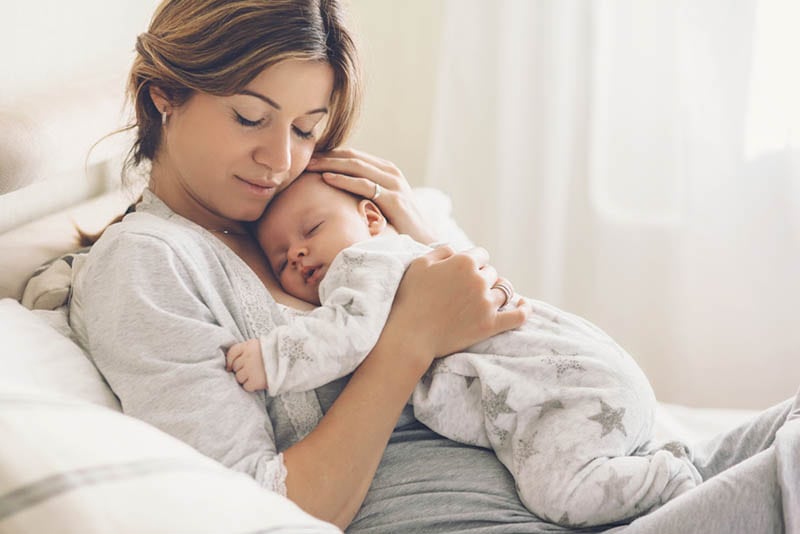 schöne junge Mutter hält schlafendes Baby auf Brust und kuscheln auf dem Bett