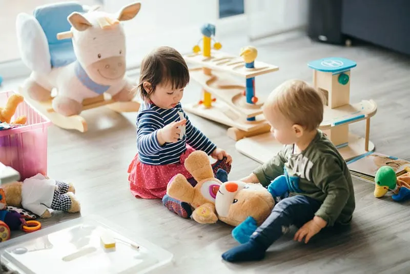 zwei niedliche Babys spielen auf dem Boden mit Spielzeug