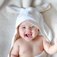 kleines Baby lachend auf dem Bett, während es in ein Badetuch mit Hasenohren gewickelt wird