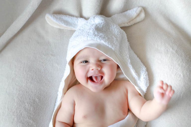 kleines Baby lachend auf dem Bett, während es in ein Badetuch mit Hasenohren gewickelt wird