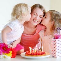 zwei kleine Mädchen geben ihrer Mutter zum Geburtstag einen Kuss auf die Wange