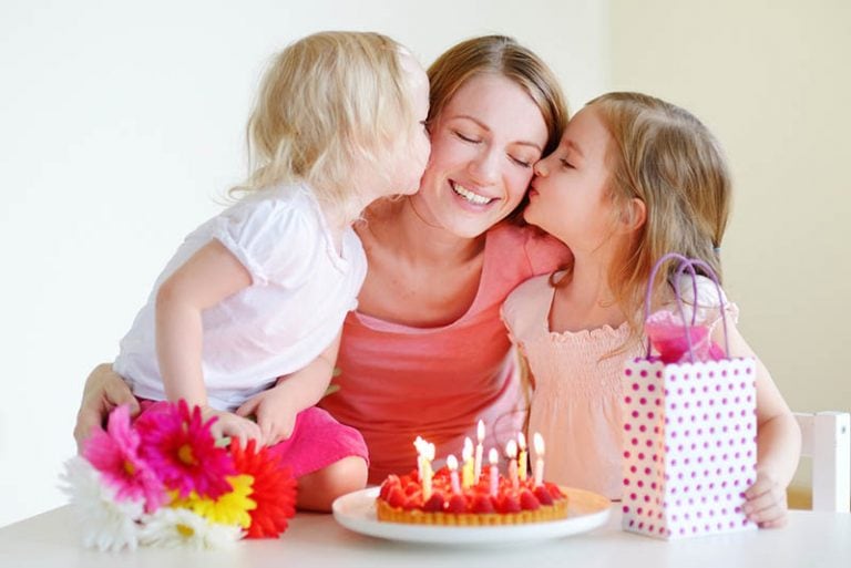 zwei kleine Mädchen geben ihrer Mutter zum Geburtstag einen Kuss auf die Wange