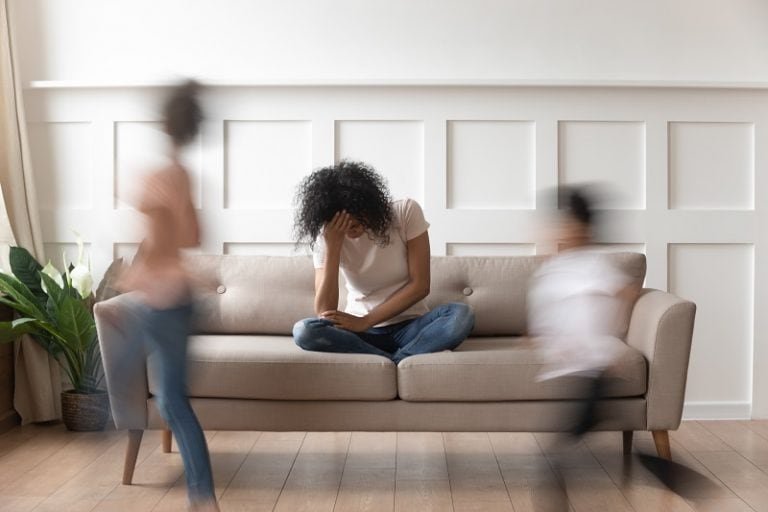 Frustrierte und wütende Mutter sitzt auf der Couch, während ihre Kinder herumlaufen