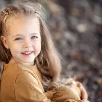 schönes kleines Mädchen sitzt auf einem felsigen Strand in einem braunen Kleid