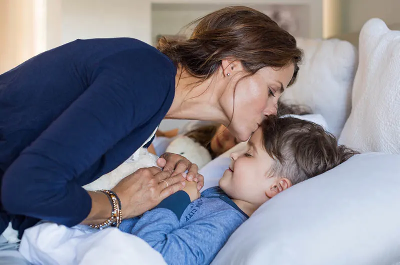 Mutter gibt dem schlafenden Sohn einen Gute-Nacht-Kuss
