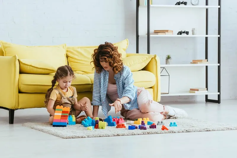 Mutter und Tochter spielen mit Bauklötzen auf dem Boden zu Hause