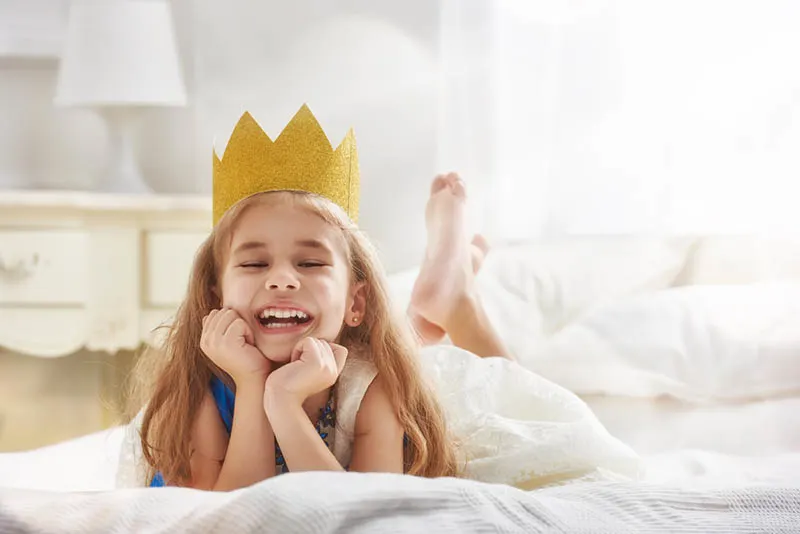 Nettes kleines Mädchen in einem Prinzessinnenkostüm mit Krone auf dem Bett liegend