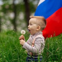 kleiner Junge spielt mit einer Blume vor einer russischen Flagge