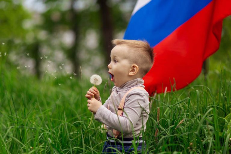 kleiner Junge spielt mit einer Blume vor einer russischen Flagge