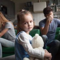 kleines Mädchen hält ein Spielzeug, während ihre Eltern durch eine Trennung gehen
