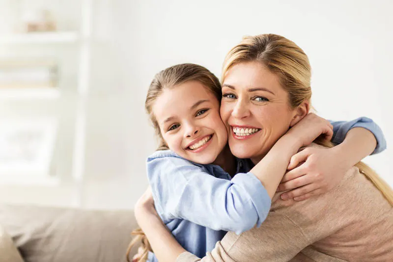 glücklich lächelndes Mädchen mit Mutter umarmt auf Sofa zu Hause