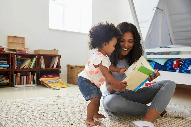 glückliche Mutter liest ein Buch mit ihrem Baby auf dem Zimmerboden