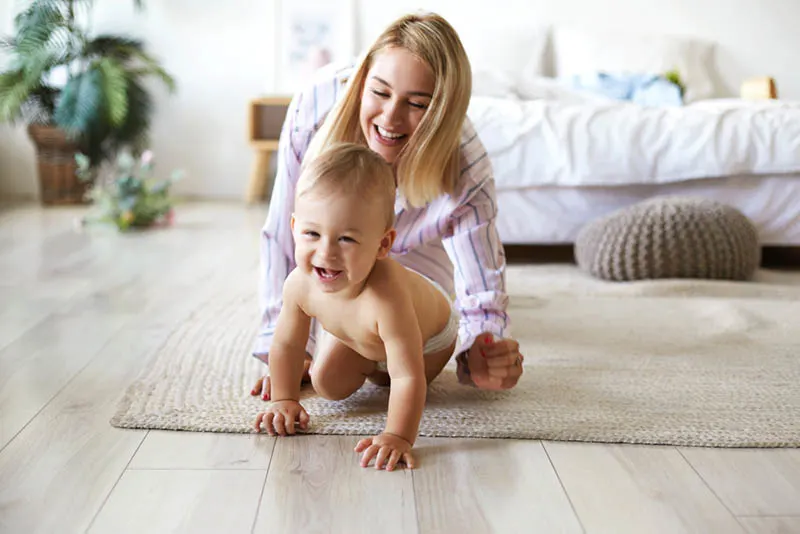 glückliche junge Mutter fängt ihr krabbelndes Baby auf dem Boden zu Hause