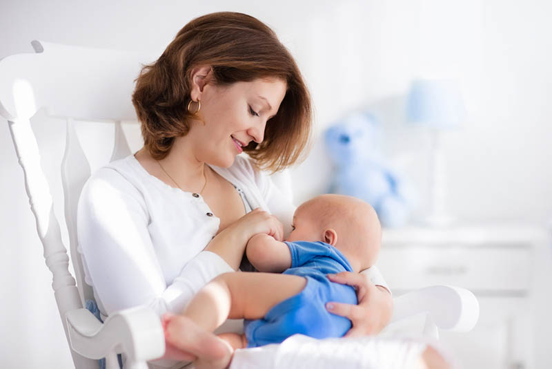junge Mutter sitzt auf einem Stuhl und stillt ihr Baby