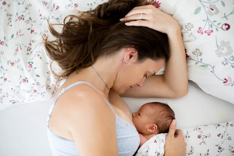 junge Mutter stillt ihr neugeborenes Baby im Bett auf floralen Laken