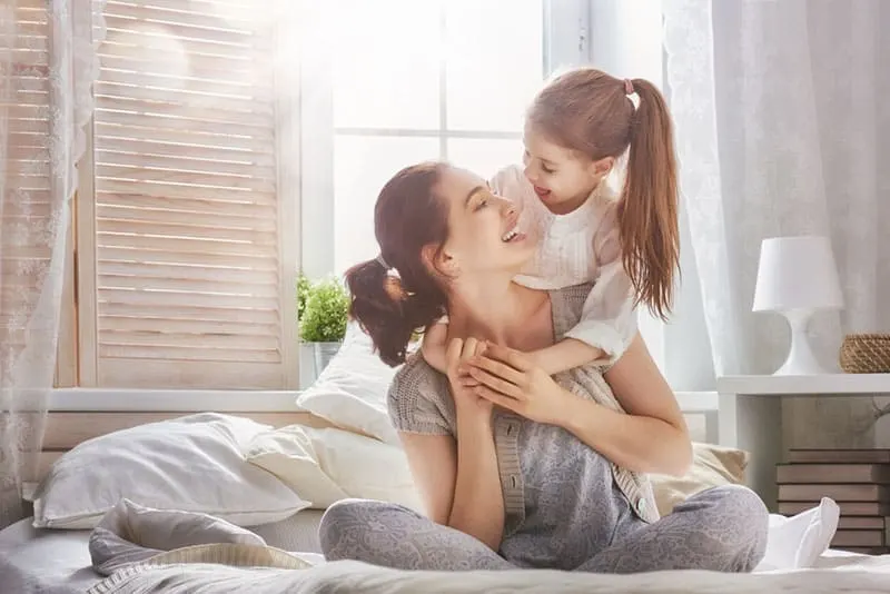 junge Mutter umarmt mit Tochter auf dem Bett