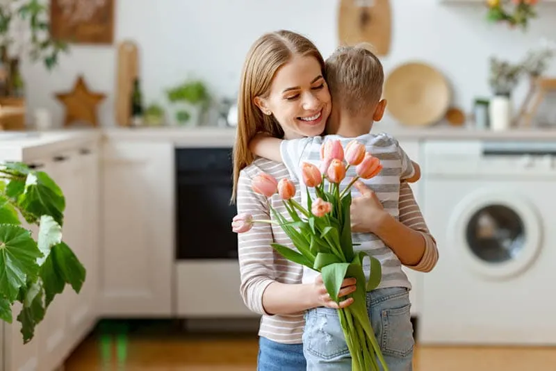 kleiner Junge umarmt seine Mutter mit Tulpen in ihren Händen