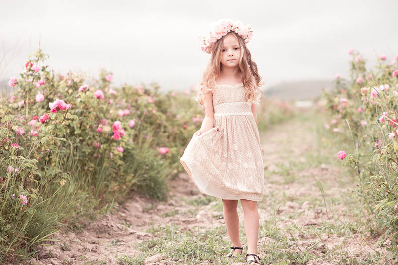 kleines Mädchen in Kleid und Blume Stirnband zu Fuß in der Blume Feld