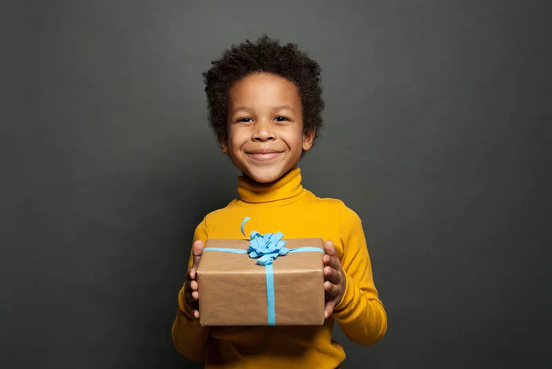 süßer kleiner Junge im gelben Rollkragenpullover lächelt und hält ein Geschenk