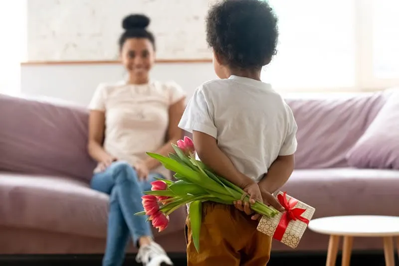 niedlichen kleinen Jungen versteckt Blumen und Geschenk vor seiner Mutter