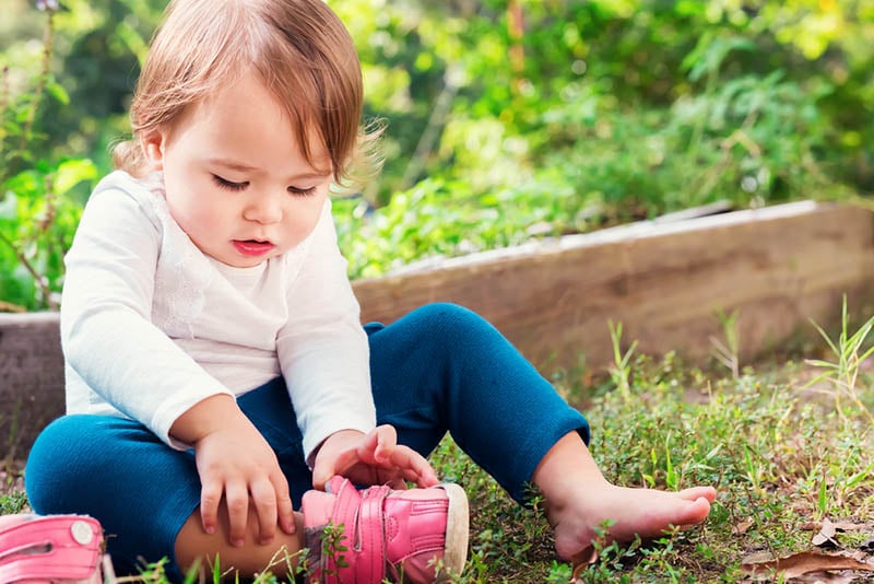 niedlichen kleinen Mädchen ausziehen ihre Schuhe im Freien auf dem Gras