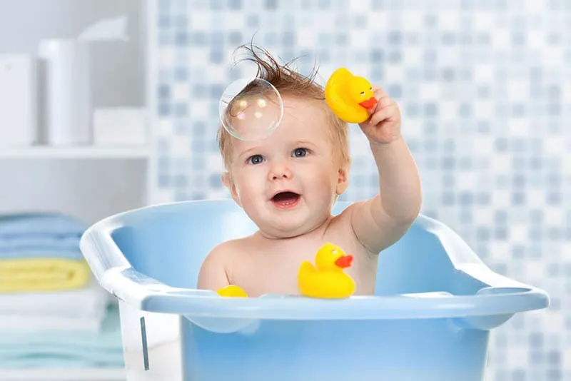 süßes Baby Junge ein Bad nehmen und spielen mit Blasen und Ente Spielzeug