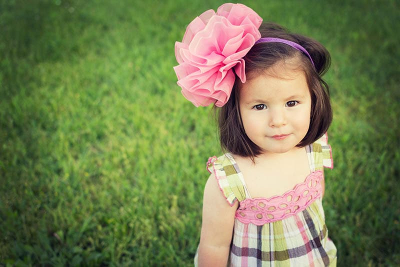 süßes kleines Mädchen mit großen rosa Stirnband im Kleid stehend auf dem Gras im Freien