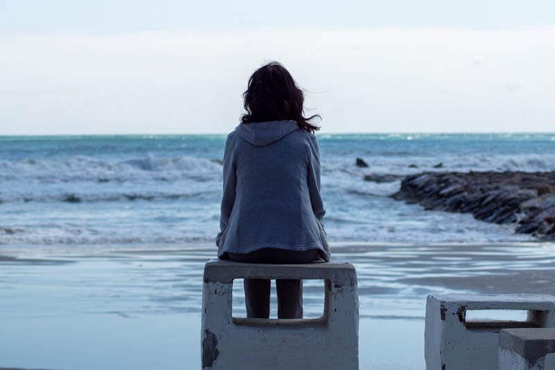 traurige Frau sitzt am Strand und schaut aufs Meer