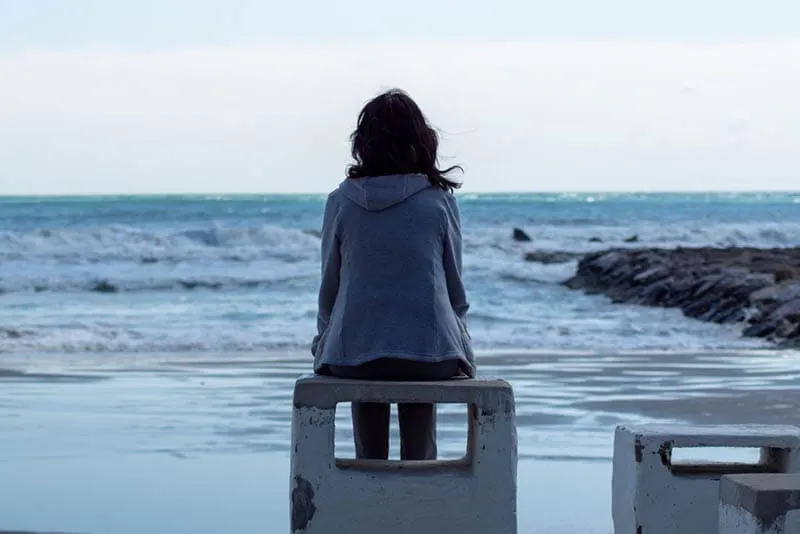 traurige Frau sitzt am Strand und schaut aufs Meer