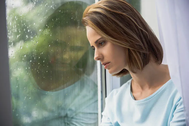 traurige Frau steht neben dem regnerischen Fenster