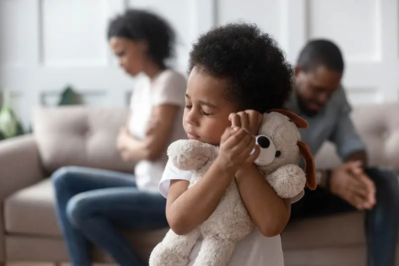 trauriger kleiner Junge umarmt Spielzeug, während Eltern im Konflikt