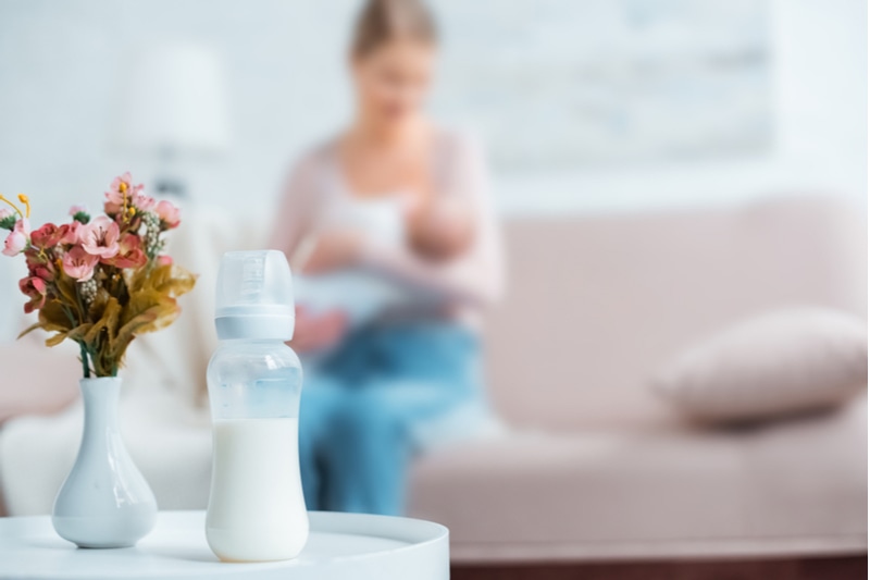 Babyflasche mit Milch - Mama und Baby im Hintergrund