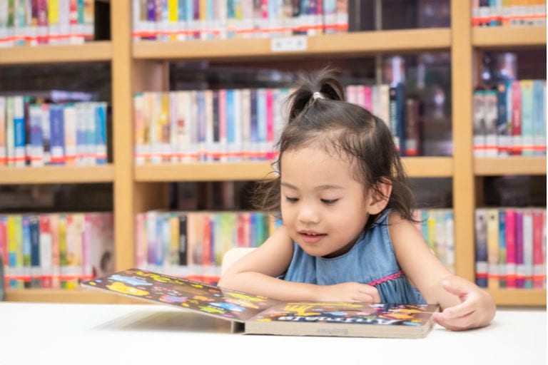 kleines Mädchen liest ein Kinderbuch in der Bibliothek