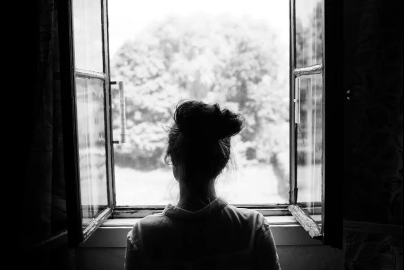 Frau schaut durch das alte Fenster