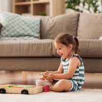 glückliches 3-jähriges Mädchen, das mit einem Holzspielzeug auf dem Boden spielt