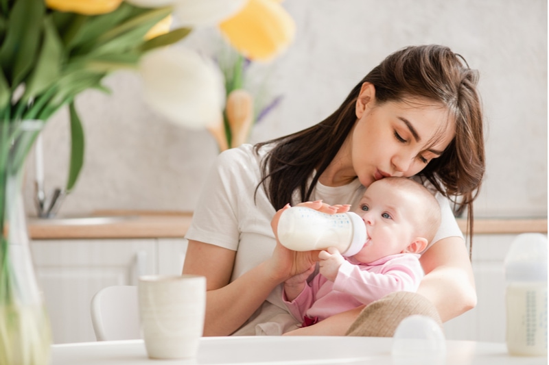 Junge Frau küsst Baby beim Trinken von Milch