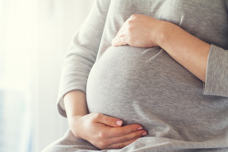 Junge schwangere Frau hält ihre Hände auf ihrem Bauch
