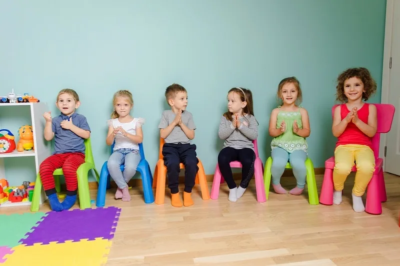 Kinder spielen ein Spiel, während sie auf bunten Stühlen sitzen