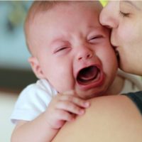 Mutter hält und beruhigt ihr weinendes Baby, das nicht trinken will