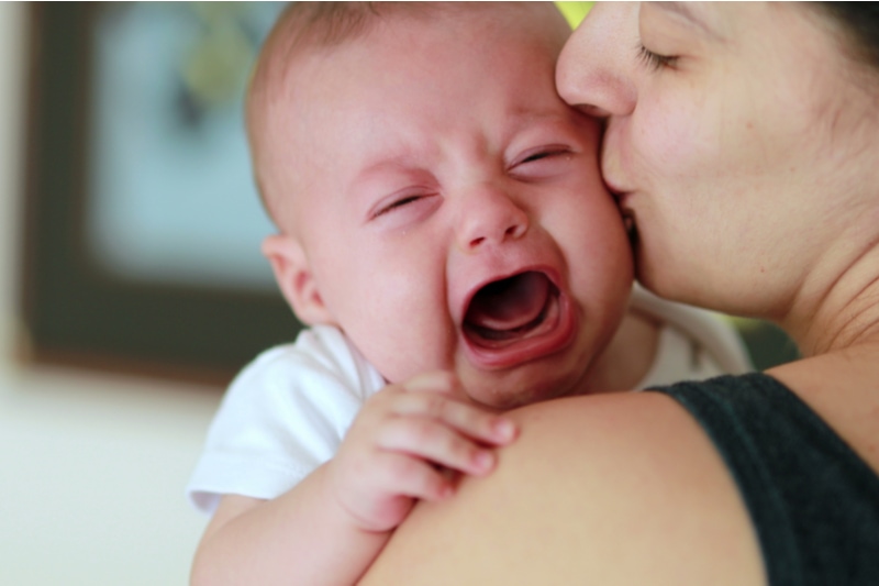 Mutter hält und beruhigt ihr weinendes Baby, das nicht trinken will