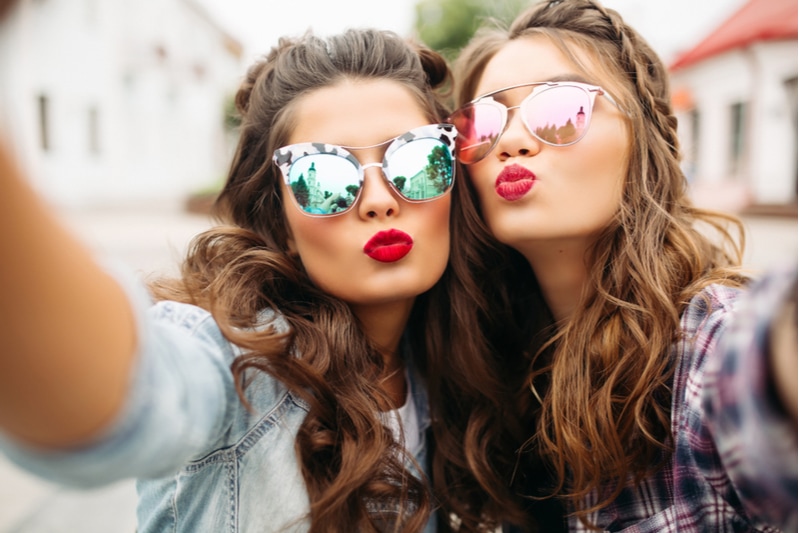 Zwei Mädchen mit roten Lippen und welligem Haar machen Selfie