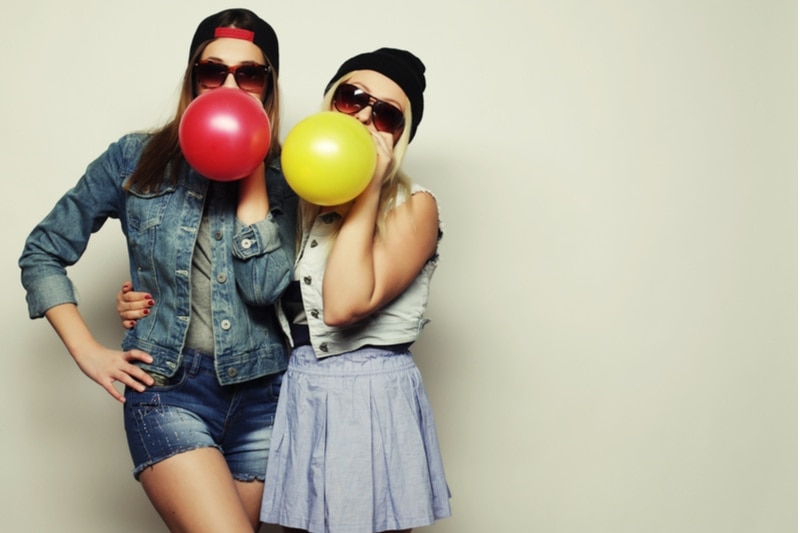 Zwei coole Mädchen mit Sonnenbrille halten bunte Luftballons