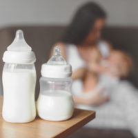 Mutter hält ihr Baby neben zwei mit Milch gefüllten Babyflaschen